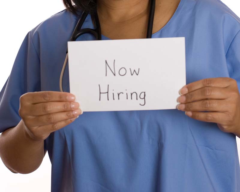 smiling nurse holding up a hiring sign