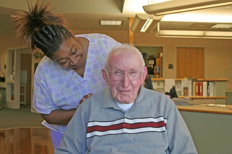 smiling friendly nurse with old man in wheelchair