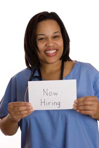 smiling nurse holding up a we're hiring sign